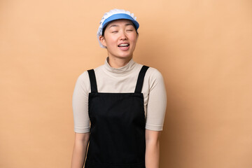 Young Chinese Fishmonger woman wearing an apron and holding a raw fish isolated on pink background laughing