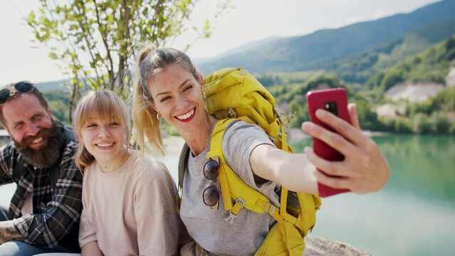 Happy family with preteen daughter on hiking trip on summer holiday, resting and taking selfie