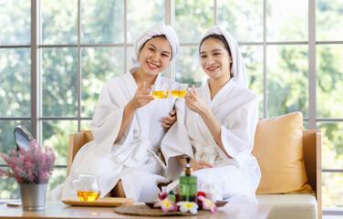 Two Asian young beautiful spa customers in white clean bathrobe covered head with towel sitting...