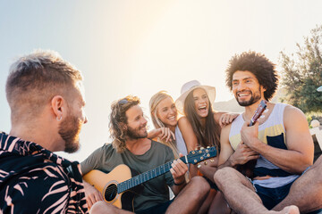 Young friends having fun and playing guitar at the beach