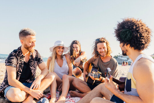 Young friends having fun and playing guitar at the beach