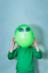 child dressed in green clothes playing alien. girl with a green ball where eyes and faces are drawn