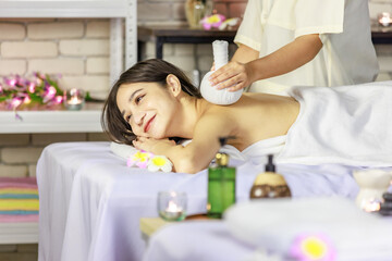 Obraz na płótnie Canvas Asian young beautiful sexy cheerful female spa customer laying down covered with white clean bath towel smiling while unrecognizable masseuse using hot herbal compress massaging shoulder and back