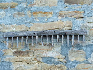old wooden rake hanging on a stone wall of a country house - 504579219