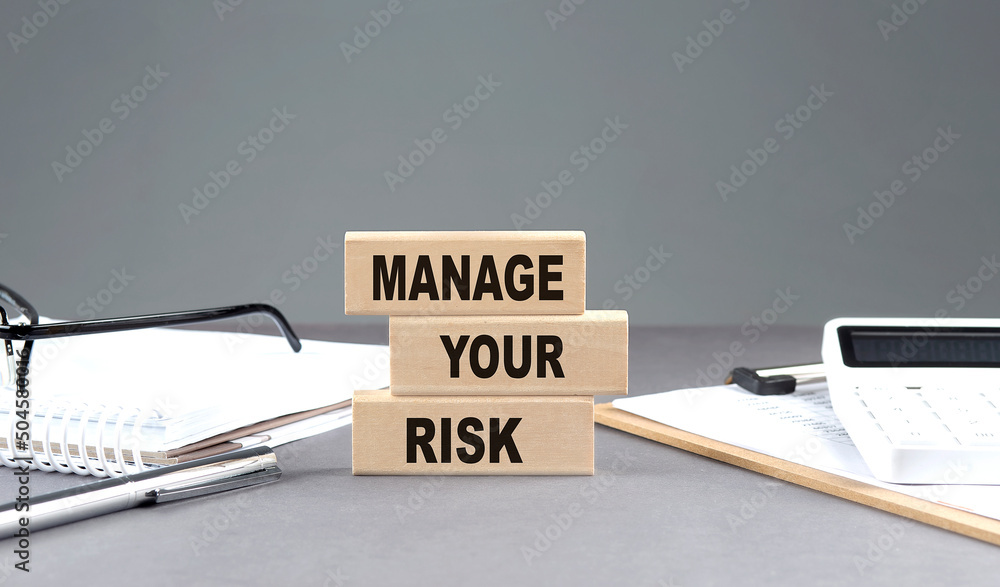 Poster manage your risk text on wooden block with notebook,chart and calculator, grey background