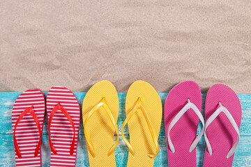 Fototapeta premium Sand copy space. Sand background top view. Multicolored beach flip flops