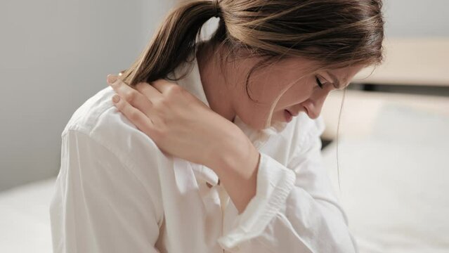Back pain, shoulder girdle spasm. Suffering woman touches and makes self-massage of upper back, trapezius muscle and neck