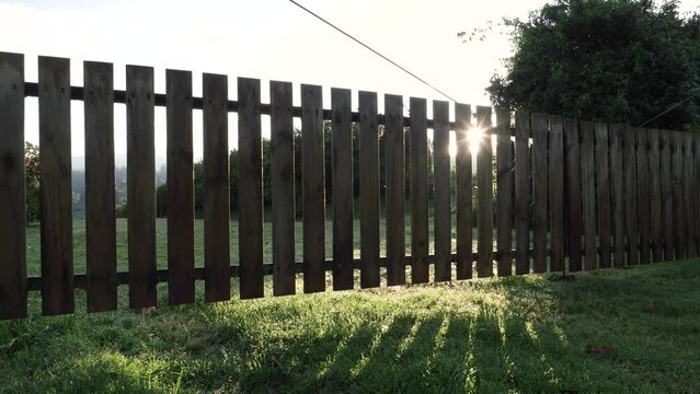 Sun shining behind a picket fence over green lawn as camera pans across