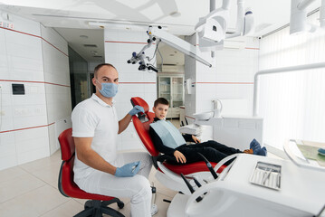 Fototapeta premium A young dentist examines and treats the teeth of an eight-year-old boy in modern white dentistry close-up. Dental prosthetics, treatment and teeth whitening. Modern dentistry. Prevention.