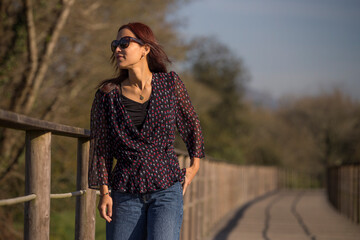 Mature and beautiful woman with sunglasses in pose isolated on a forest background with sunset colors.