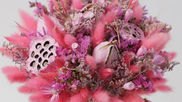 Pink bouquet of different beautiful dried flowers rotates around the axis on a white background