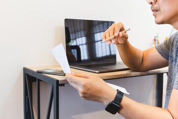 Man reading document paper while working on laptop at home.