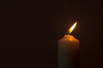 A single burning candle flame or light glowing on a white candle on black or dark background on...
