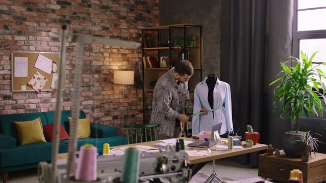 Ravishing looking man, nicely dressed is doing up measurements on a mannequin and working very hard as he is designing clothes