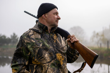 Hunter with a gun on his shoulder on a background of misty morning lake. Close up