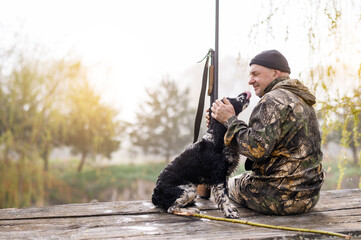 Male hunter sits on a bridge against the backdrop of sunrise and forest with a lake with a Russian...