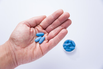Male hand showing three pills in the palm and in the background a container full of blue tablets - 504592081