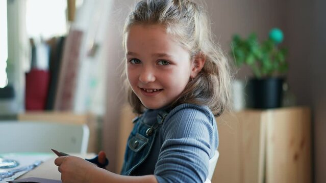 Happy little girl cutting paper with scissors during creative art and craft class at school.