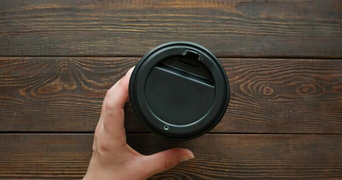 Glass of coffee to go on a wooden brown background. Pouring black coffee. The hand takes a paper cup. 4K stop motion animation
