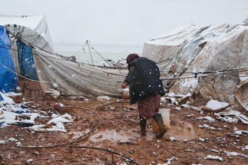 A refugee woman walking in a snowy atmosphere, Syrian refugees in winter.	