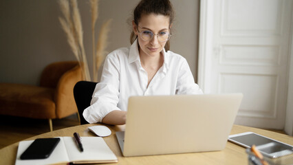 A woman with glasses is a freelancer working in an office using a laptop, making a project report