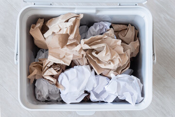 Top view: sorting of garbage - white and brown paper in grey recycling bin, filling garbage basket...