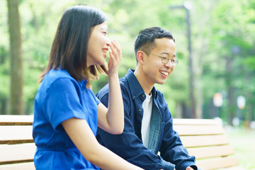 公園のベンチで談笑する若いカップル