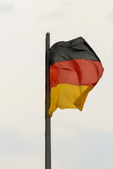 Close up of the national flag of Germany on Reichstag rooftop in summer waving high in the air. Black, red and gold horizontal stripes. Cloudy blue sky in background. No people.