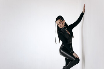 beautiful brunette in a black tight latex suit posing on a gray background - obrazy, fototapety, plakaty
