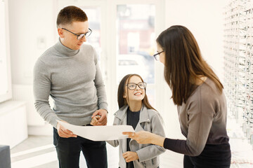 Optometrist helping family choosing glasses in optics store