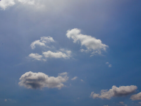 white cloud tufts illuminated by sunlight floating under a misty blue sky.