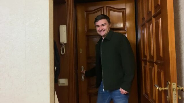 Cheerful adult male enters apartment through front door and celebrates good news