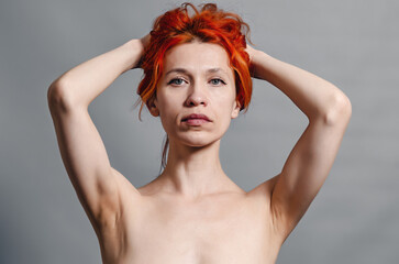 Red naked woman. Hands near the hair. Blue eyes. Relax. Front view. Gray background.