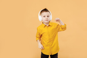 portrait of funny clever school boy with headphones in yellow shirt. Yellow studio background. Education. Looking and smiling at camera