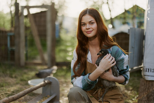 Young woman smiling for the camera holding a chicken and happy working on the farm