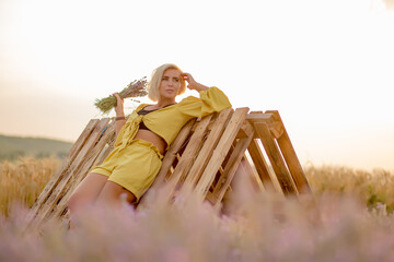 Pretty young woman in yellow among rural field with golden oat field on sunset background