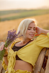 Pretty young woman in yellow among rural field with golden oat field on sunset background