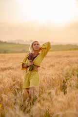 Pretty young woman in yellow among rural field with golden oat field on sunset background