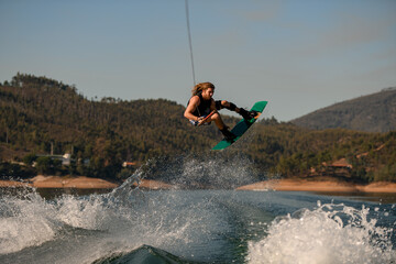 man with wakeboard masterfully jumping high over splashing wave.