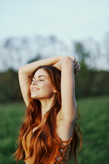 A woman warms up and stretches her arms up in nature in a green park after an outdoor sports workout in the sunset sunlight. The concept of a healthy lifestyle and an athletic body