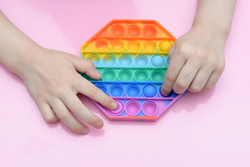 popular toy multi-colored pop it in the form of an octahedron in the hands of a child on a pink background