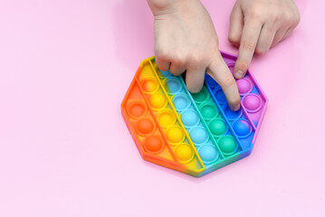 popular toy multi-colored pop it in the form of an octahedron in the hands of a child on a pink background