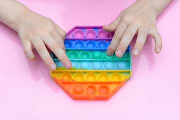 popular toy multi-colored pop it in the form of an octahedron in the hands of a child on a pink background