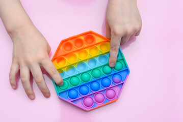 popular toy multi-colored pop it in the form of an octahedron in the hands of a child on a pink background