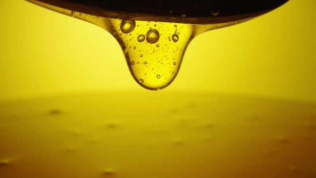 Drops of thick golden honey flowing down on a yellow background. Close up of sweet nectar or molasses being spilled. Liquid honey pours and drips. Sugar syrup is pouring. Healthy and curative dessert.
