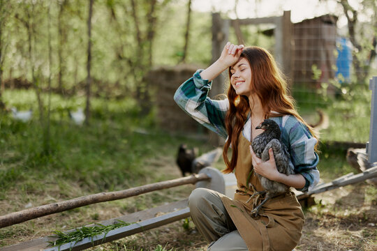 A woman examines a chicken in her hands and rubs her forehead from the fatigue of working on a farm and caring for the birds she feeds organically