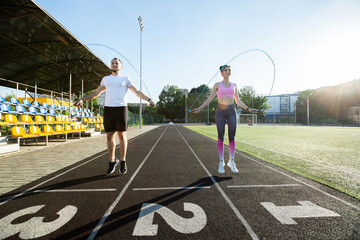 Young fitness couple exercising outdoors at sunset - jumping with skipping rope