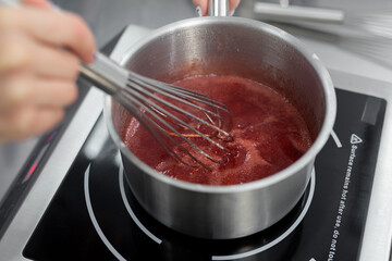 Pastry chef cooks strawberry puree with sugar in a saucepan