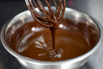 Pastry chef whips melted chocolate in a bowl with a metal wire whisk close up