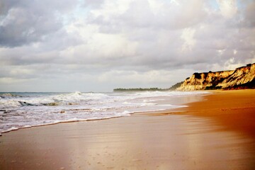 White waves crashing  the beach, in the calm ocean. Horizon cloudy with morning light. Far away yellow cliffs on the shore